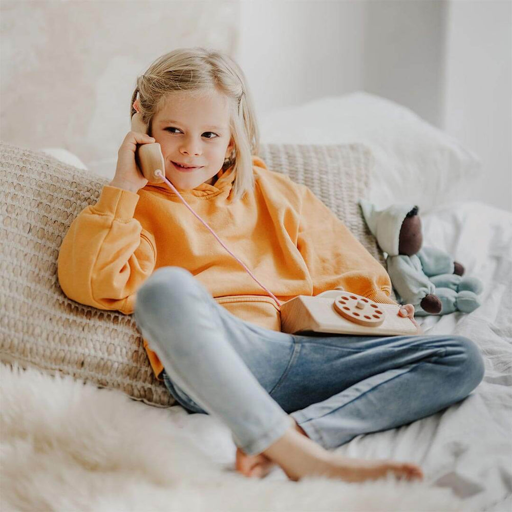 Child sitting on couch with Grimm's Wooden Telephone