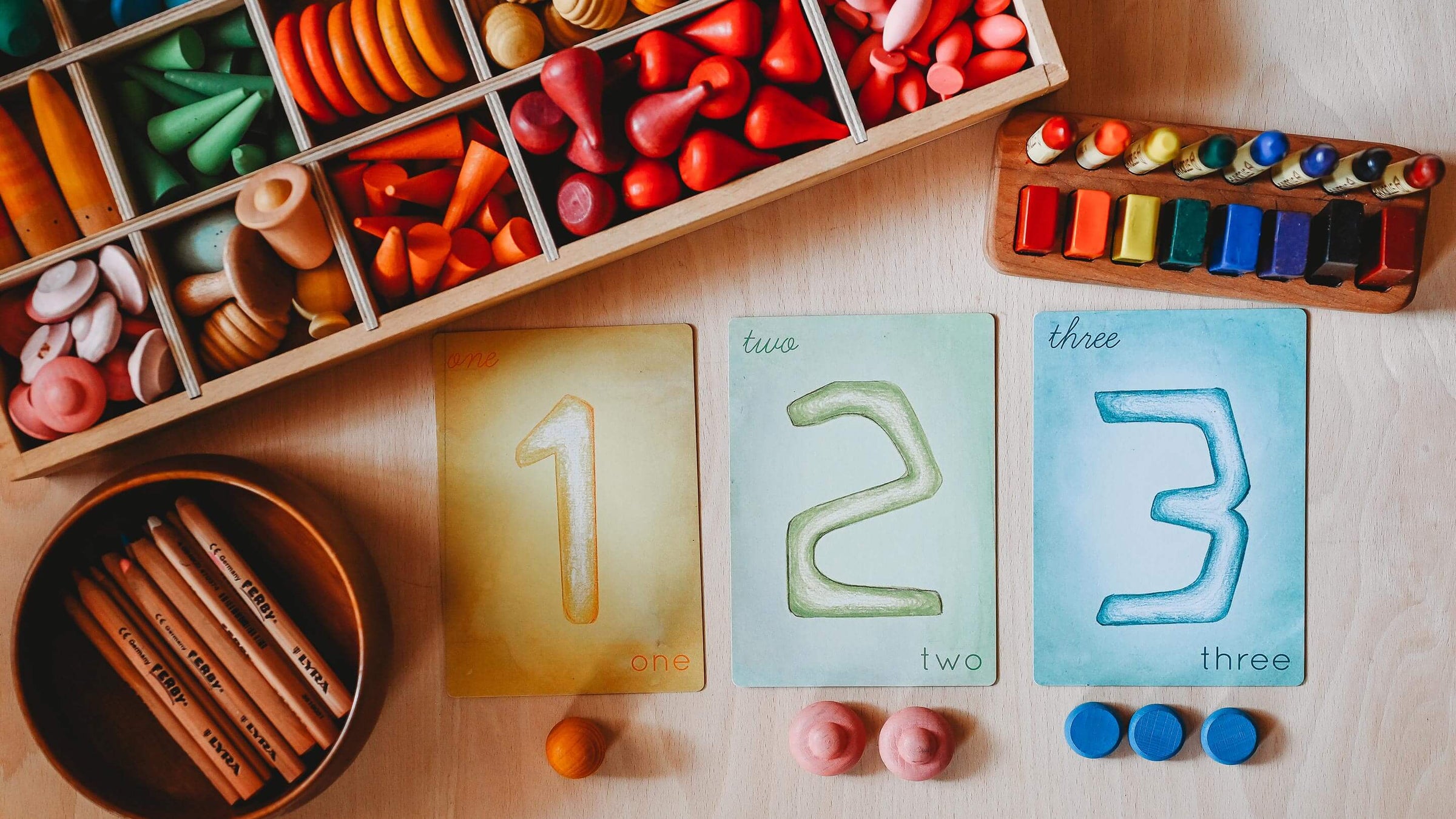 1, 2, and 3 Number Cards on a wooden table with wooden toys in a box and a set of crayons